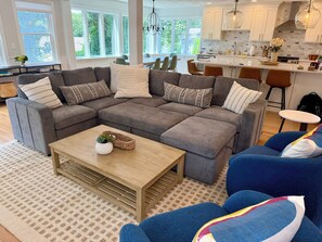 A modern living room with a sectional sofa, a coffee table, and a view of the kitchen and dining area. - 3-bedroom Coastal Narragansett Escape located in the heart of South County (Narragansett)