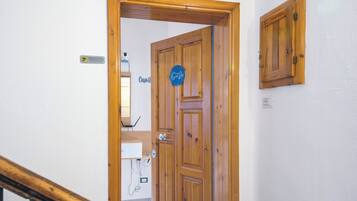 Eine Holztür mit einem Schild, ein Fliesenboden und ein kleines Schränkchen an der Wand.