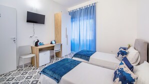 A hotel room with two beds, a desk, a chair, a TV mounted on the wall, and a window with curtains.