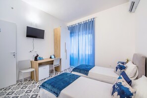 Een hotelkamer met twee bedden, een bureau, een stoel, een aan de muur bevestigde televisie en een raam met gordijnen.