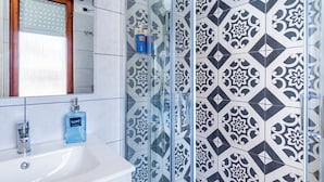 A bathroom with a glass shower enclosure, a white sink, and patterned tiles.