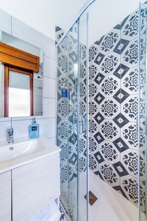 Een badkamer met een douchecabine van glas, een wit wastafelmeubel en betegelde vloeren.