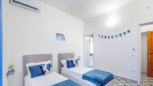 A hotel room with two beds, a wall-mounted air conditioner, a small shelf with a plant, and a patterned floor.