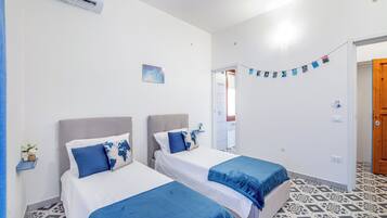Ein Hotelzimmer mit zwei Betten, einer Wand-Klimaanlage, einer kleinen Ablagefläche mit einer Pflanze und einem gemusterten Boden.