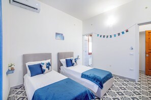 Een hotelkamer met twee bedden, een wandairconditioner, een klein plankje met een plant en een kamer met een patroon vloer.