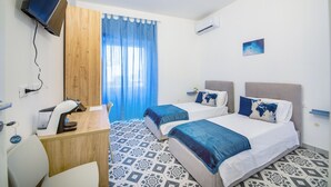 A hotel room with two beds, a desk, a chair, a TV, and a window with curtains.