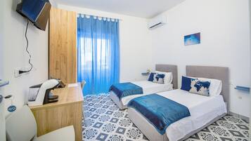 Ein Hotelzimmer mit zwei Betten, einem Schreibtisch, einem Sessel, einem Fernseher und einem Fenster mit Vorhängen.