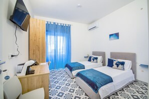 Een hotelkamer met twee bedden, een bureau, een stoel, een televisie en een raam met gordijnen.