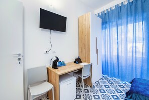 A hotel room with a bed, a desk with a laptop, a coffee maker, and a TV mounted on the wall.