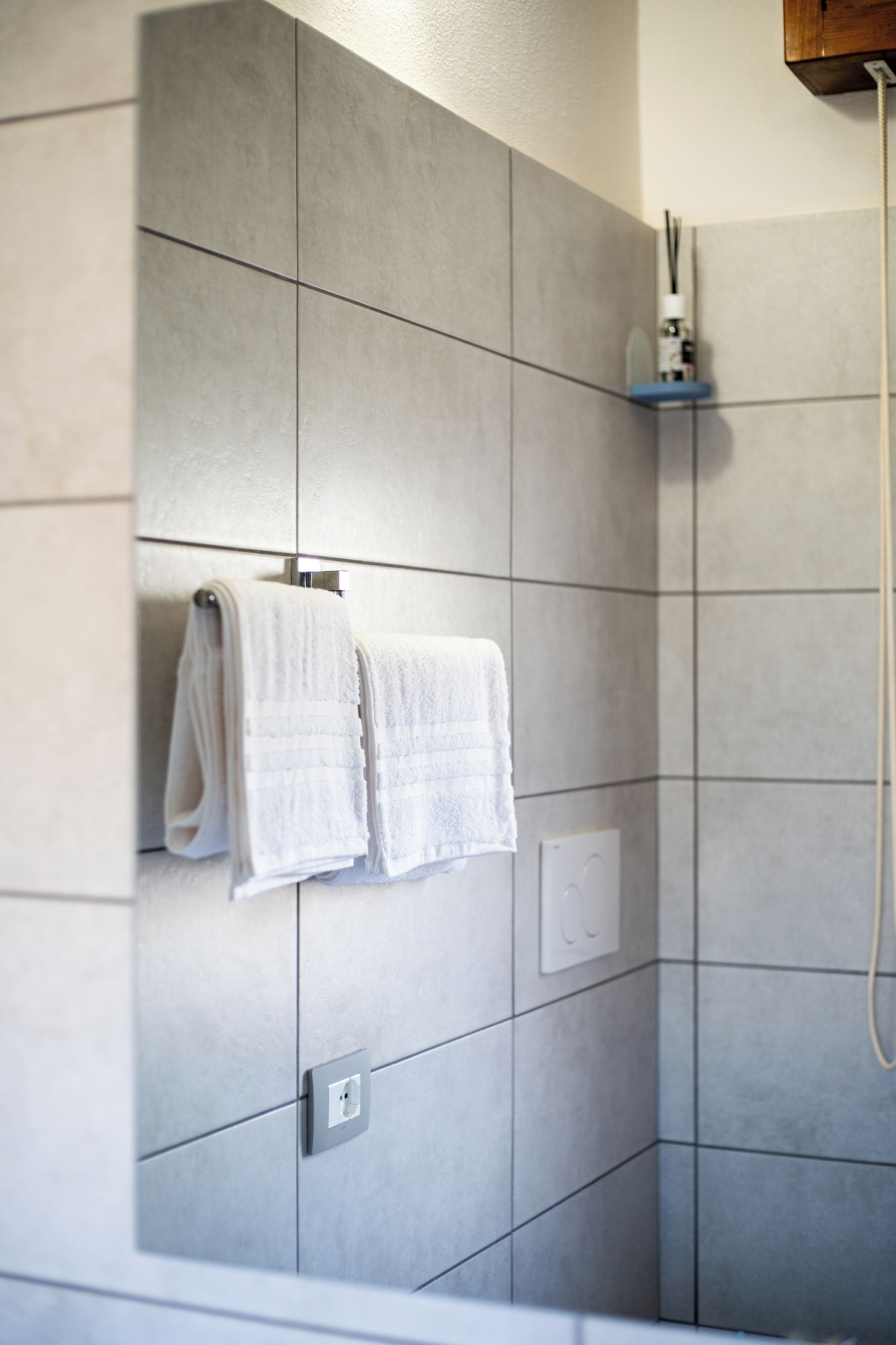 Casa de banho com azulejos cinzentos, um porta-toalhas com duas toalhas e um painel de comando do chuveiro.