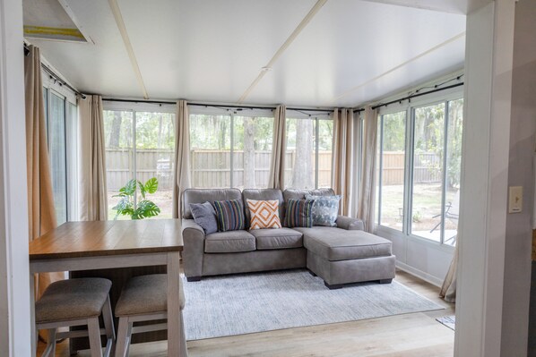 A modern living room with a grey sectional sofa, a wooden dining table, and a grey rug.