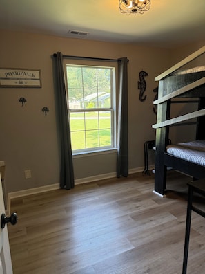 A room with a bunk bed, a window with curtains, a wall-mounted sign, and a door. - The Palmetto Blue Cottage Just Minutes to Parris Island! (Port Royal)