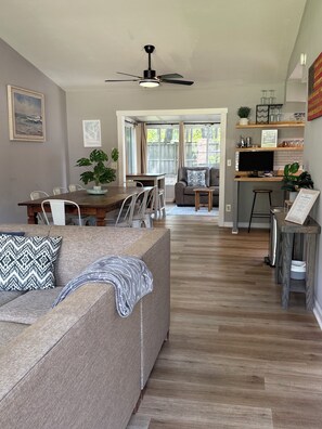 A modern living room with a sofa, a dining table, and a kitchen area with a TV and shelves.