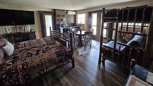 A room with a bed, a dining table with chairs, a kitchen area, and a loft bed with a view.
