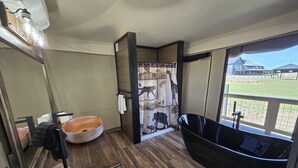 A bathroom with a wooden floor, a round sink, a black bathtub, and a shower curtain with a wildlife print.