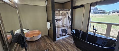 Ein Badezimmer mit Holzboden, einem runden Waschbecken, einer schwarzen Badewanne und einer Duschkabine mit einem Motiv aus Tierwelt.