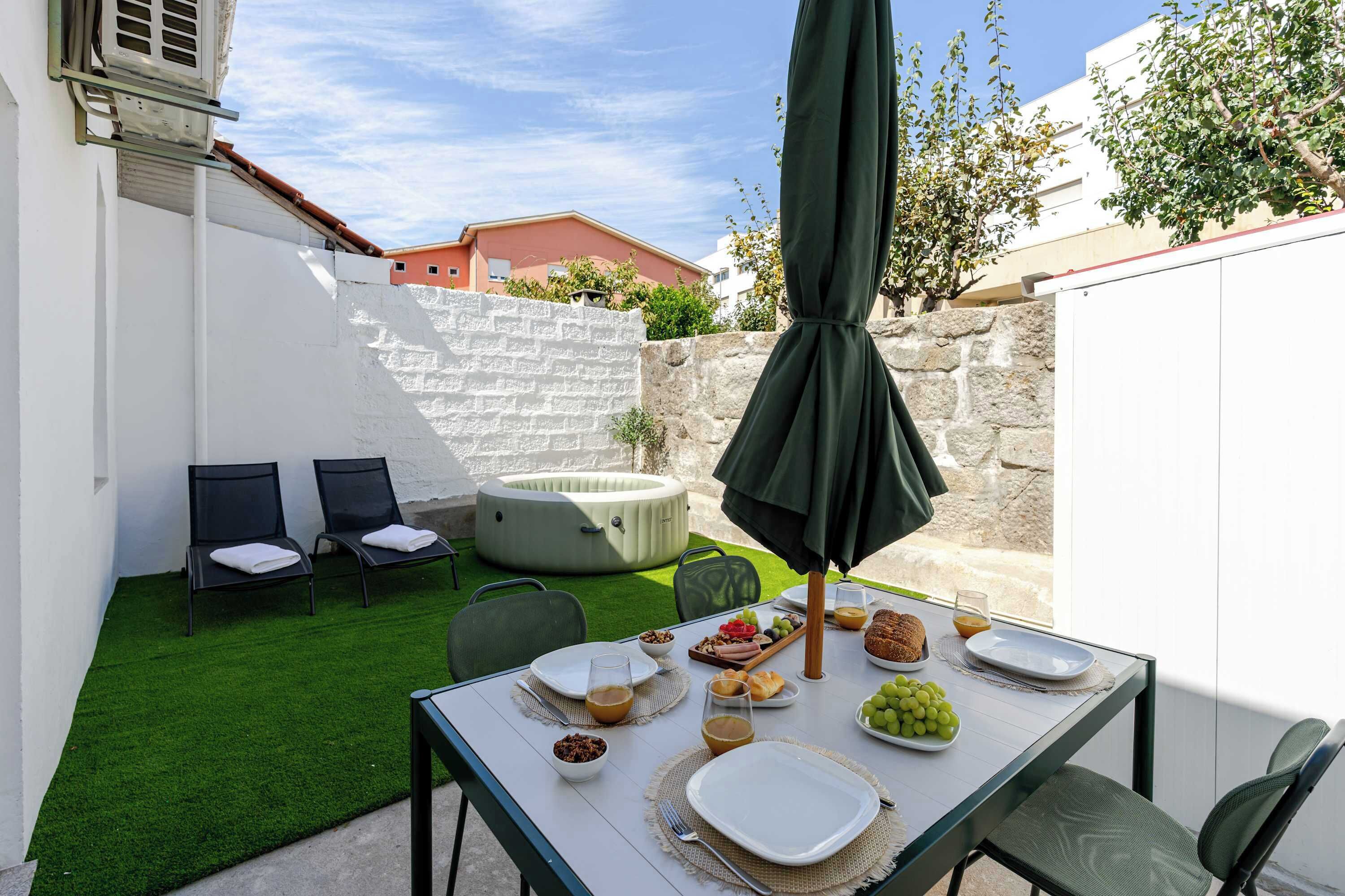 Un patio con mesa lista para el desayuno, sillas, un jacuzzi y un muro de piedra.