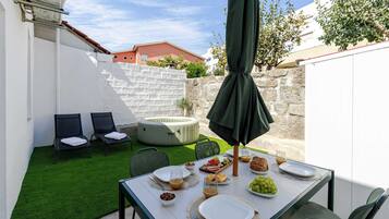 Un patio con mesa lista para el desayuno, sillas, un jacuzzi y un muro de piedra.