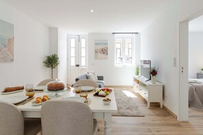 Una sala de estar moderna con comedor, que cuenta con un ventanal grande, un televisor de pantalla plana y una mesa de comedor dispuesta con comida y bebidas.