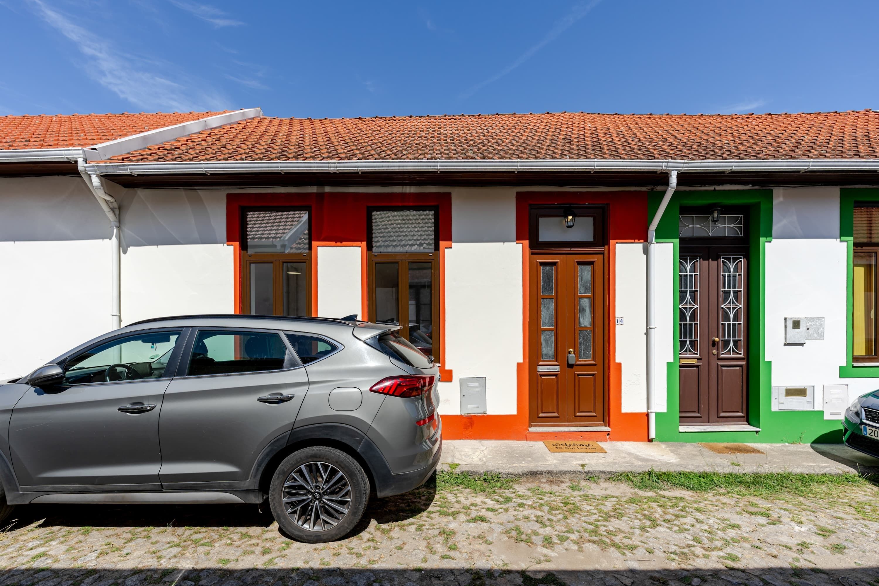 Un edificio con techo de tejas, un coche estacionado al frente y una zona con césped.