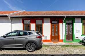 Un edificio con techo de tejas, un coche estacionado al frente y una zona con césped.
