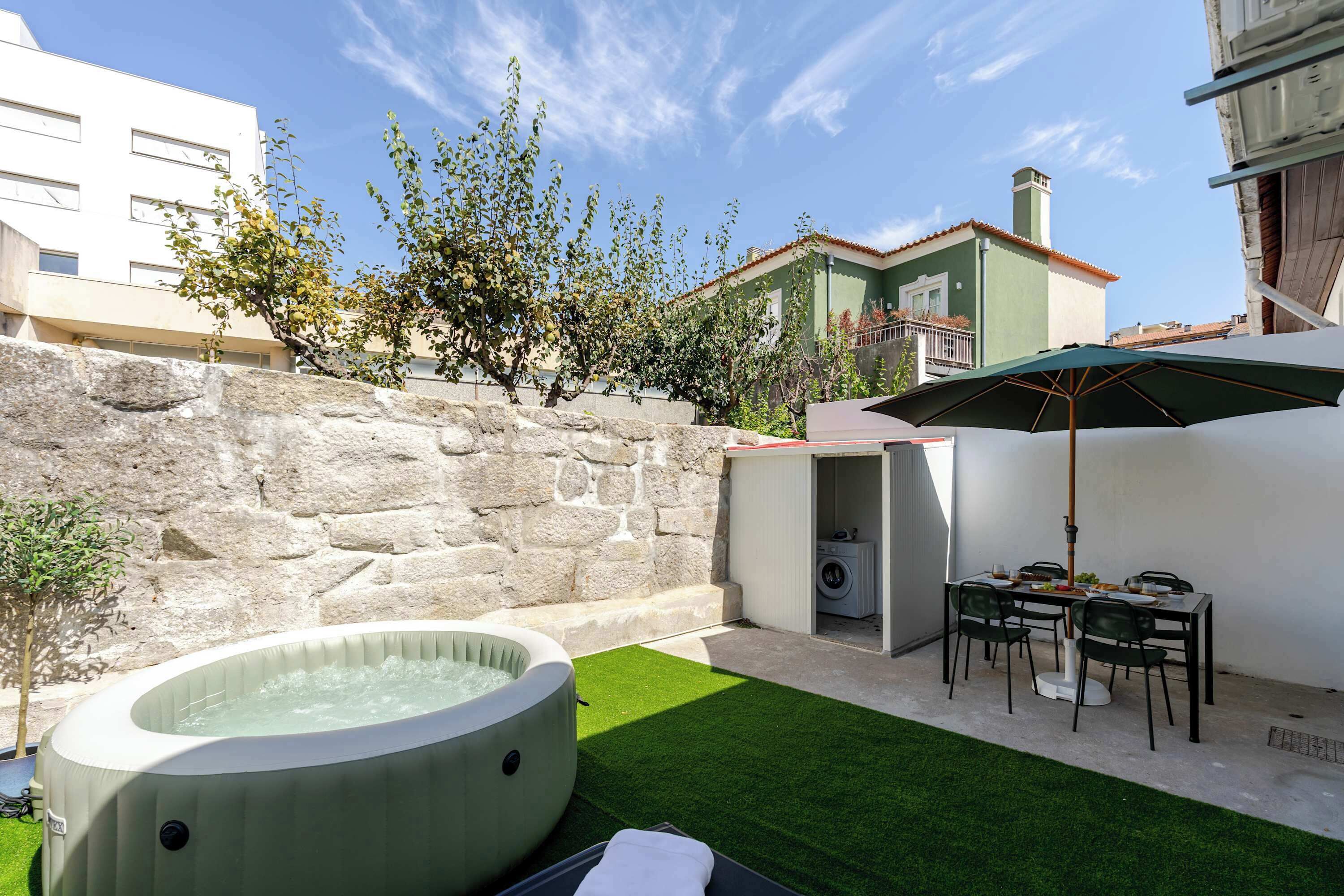 Un patio trasero con un jacuzzi, una mesa con sillas y un muro de piedra.