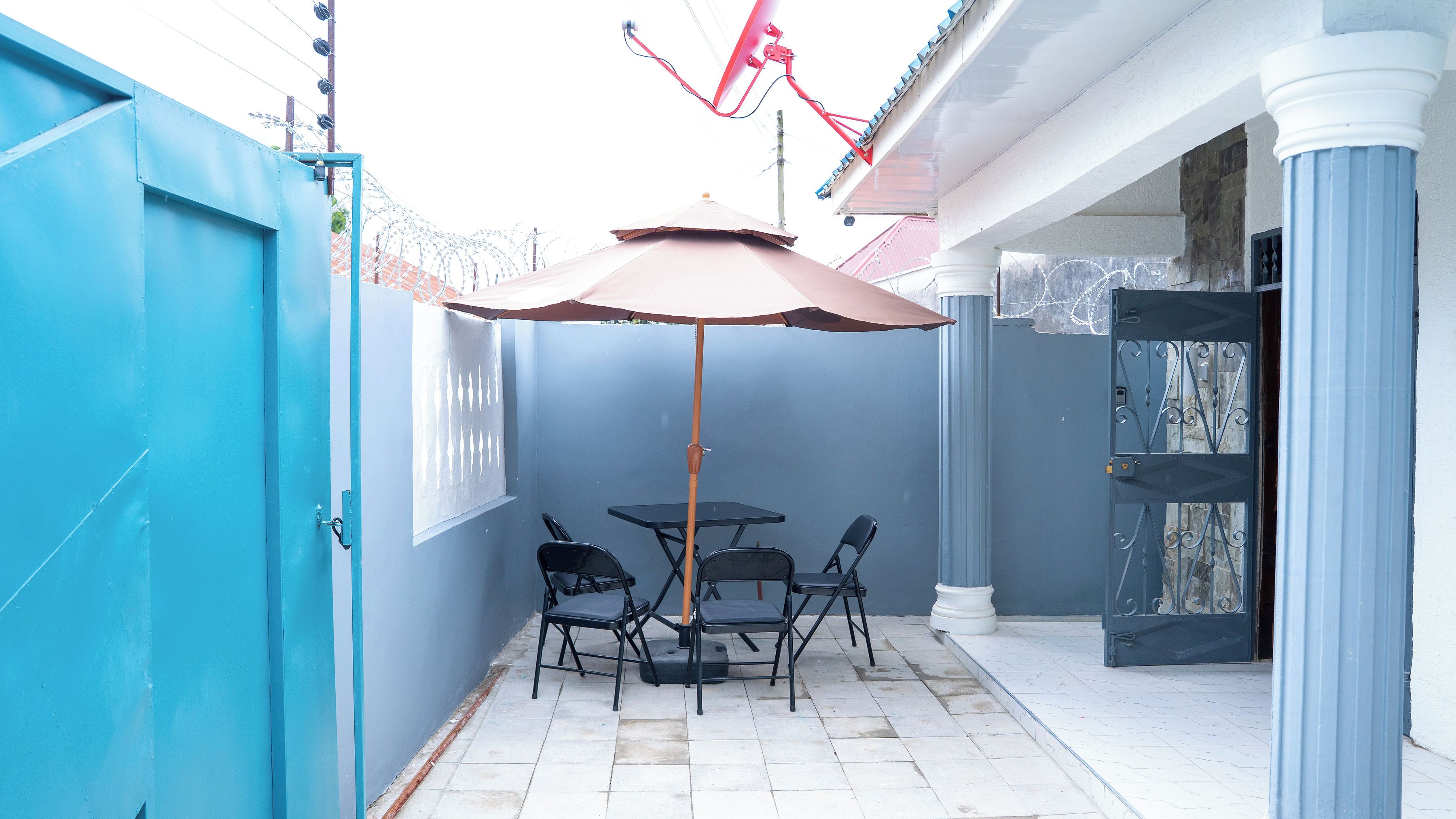 Un patio al aire libre con una mesa, sillas y un paraguas grande, además de una cerca azul.