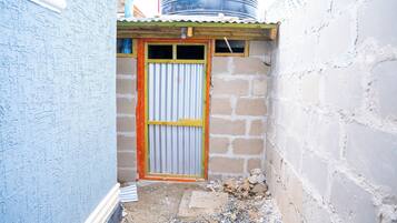 Un viottolo stretto con una porta in lamiera ondulata, una piccola struttura in legno sopra e un muro di mattoni alla destra.