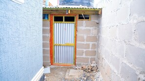 A narrow alleyway with a corrugated metal door, a small wooden structure on top, and a brick wall on the right.