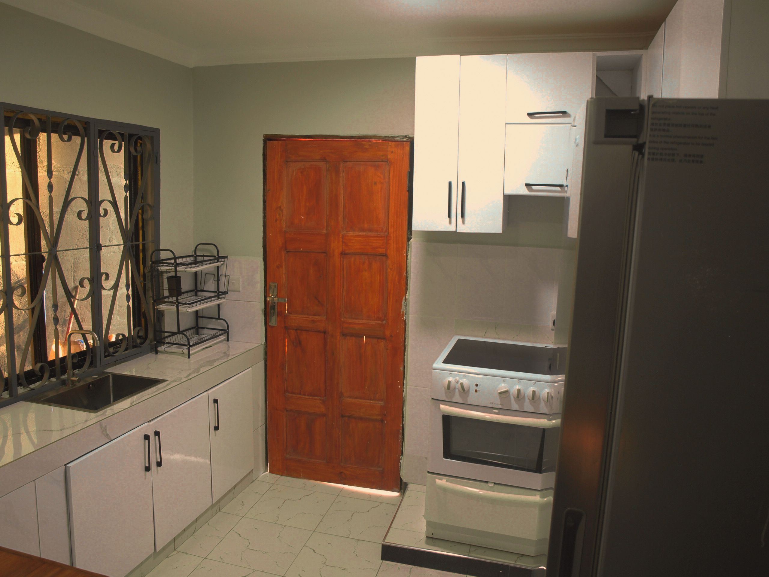 Una cocina con puerta de madera, armarios blancos, refrigerador de acero inoxidable y horno empotrado.