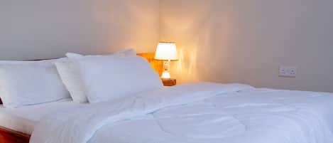 A neatly made bed with white bedding in a room with plain walls and a tiled floor.
