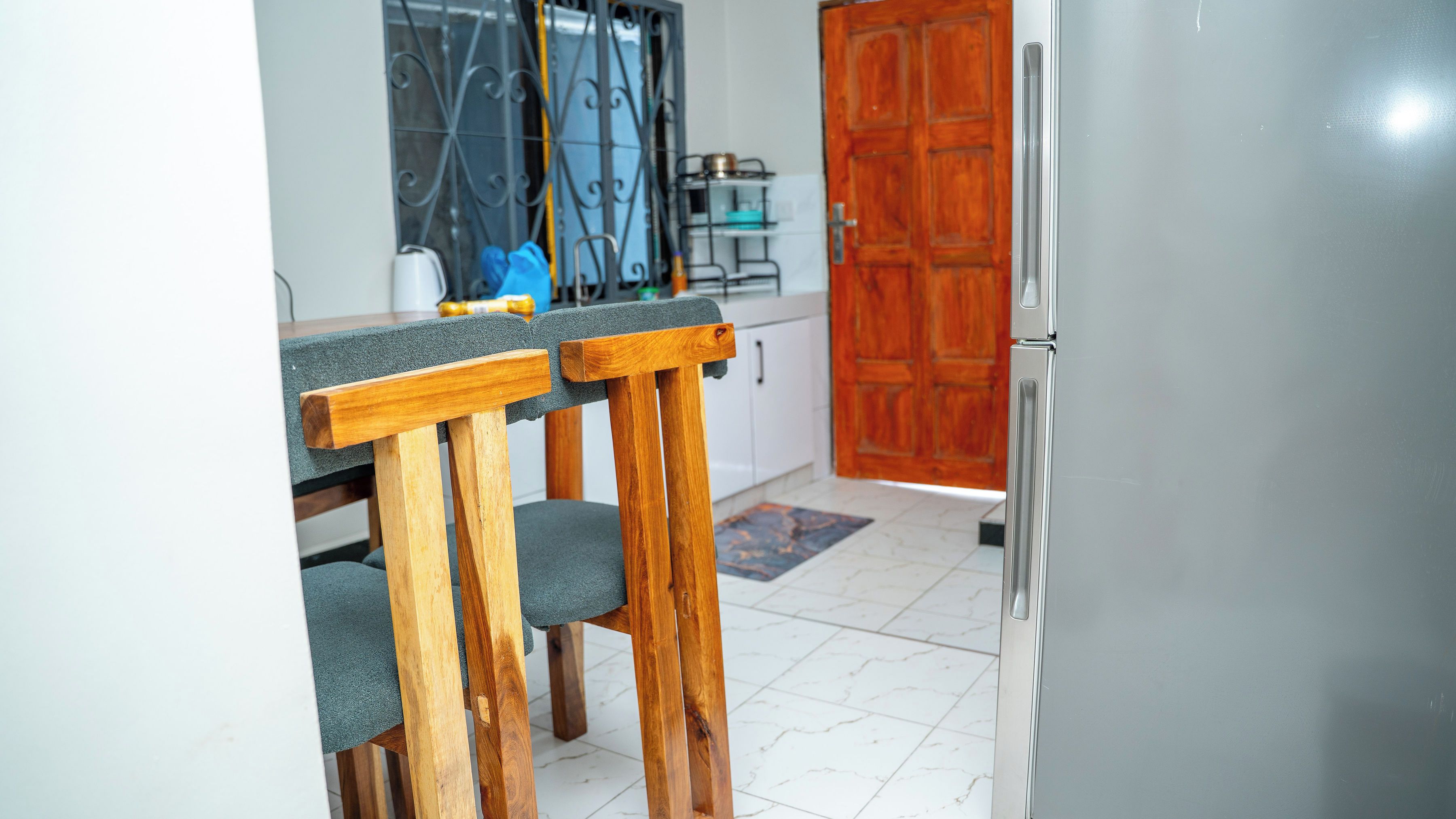 A kitchen with a wooden dining table, chairs, a refrigerator, and a wooden door.