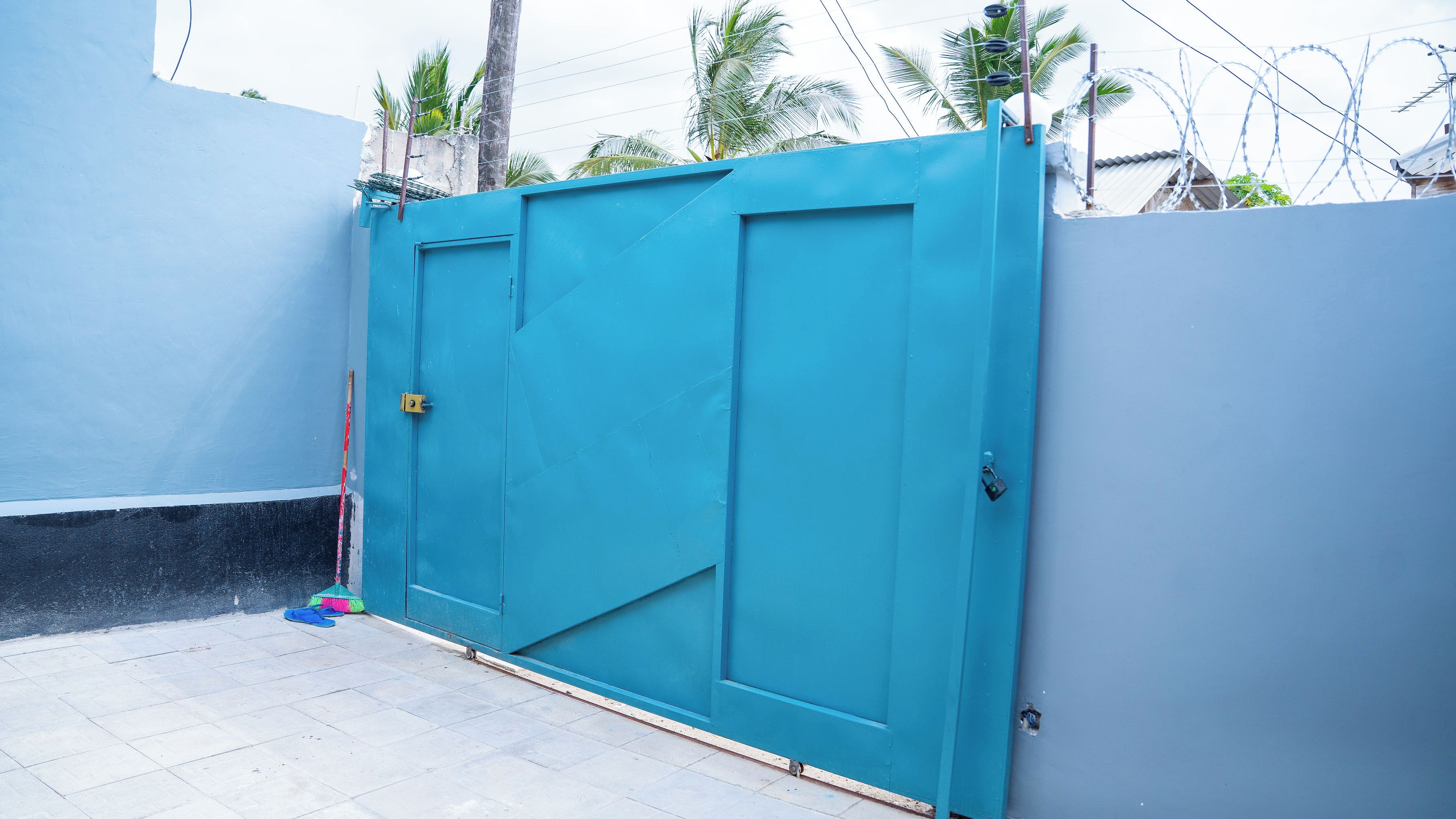A blue gate with a padlock, a white wall, and a tiled floor.