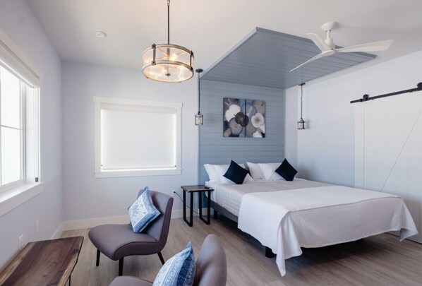 A modern bedroom with a bed, a chair, a desk, and a ceiling fan.