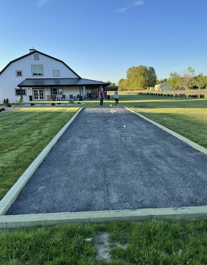 A courtyard with a croquet field, a white building with a dark roof, and a grassy area with trees.