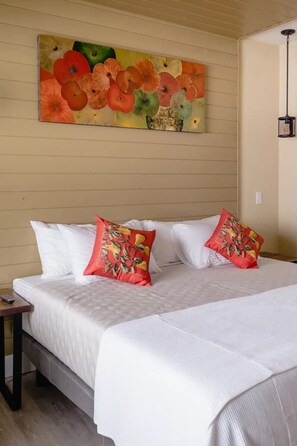 A bed with white linens and two red pillows with a tropical print, a wall with a colorful abstract painting, and a hanging light fixture. - Brix Suite at The Barn | Boutique Hotel (Walla Walla)