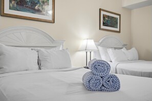 A hotel room with two beds, white bedding, a lamp, and two framed pictures on the wall. - Ocean Walk Resort 709 (Daytona Beach)