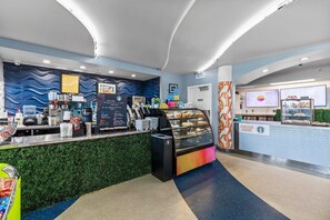 A coffee shop interior with a counter, coffee machines, and a display case. - Ocean Walk Resort 709 (Daytona Beach)