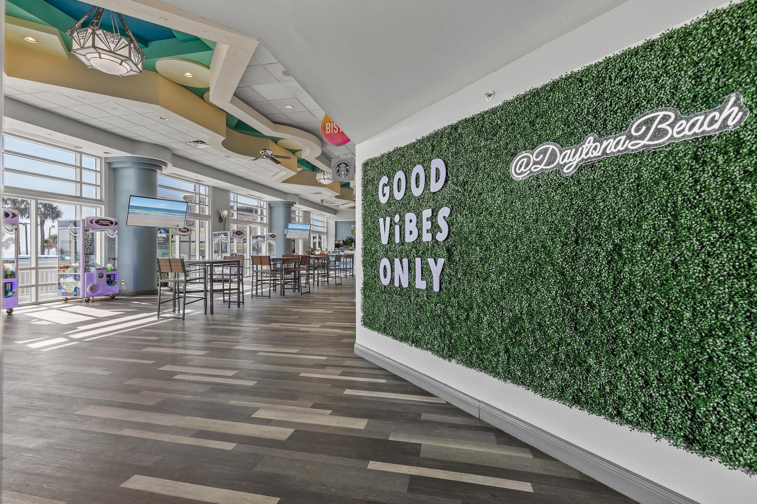 Un vaste espace intérieur dont un mur est décoré de plantes et sur lequel on peut lire l’inscription « SEULEMENT LES BONNES VIBES » et « @DaytonaBeach ».