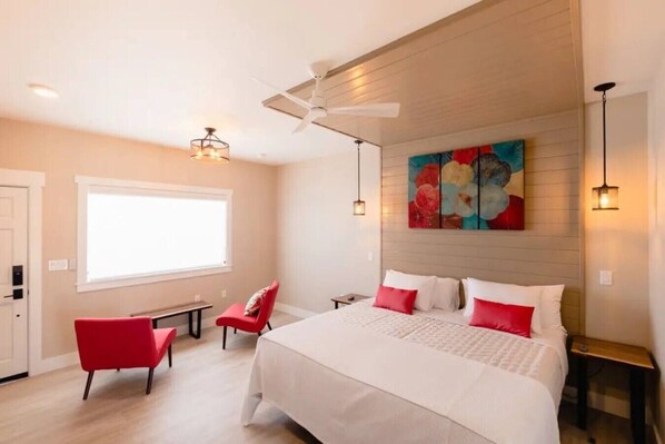 A hotel room with a large bed, a red chair, a ceiling fan, and a painting on the wall. - Vendange Suite at The Barn | Boutique Hotel (Walla Walla)