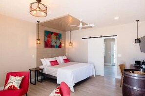 A bedroom with a bed, a chair, a table, a painting, and a ceiling fan. - Vendange Suite at The Barn | Boutique Hotel (Walla Walla)