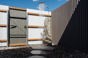 A metal gate with a water feature, a stone wall, and a gravel pathway.