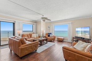 A spacious living room with a large window overlooking the ocean, furnished with leather sofas and a flat-screen TV. - Seascape Towers 1025 (New Smyrna Beach)