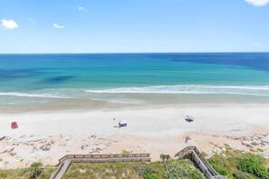 A beach with a wooden boardwalk leading to a sandy area with a few beach umbrellas and a lifeguard stand. - Seascape Towers 1025 (New Smyrna Beach)