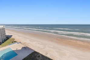 A beach view with a swimming pool and a building in the background. - Seascape Towers 1025 (New Smyrna Beach)