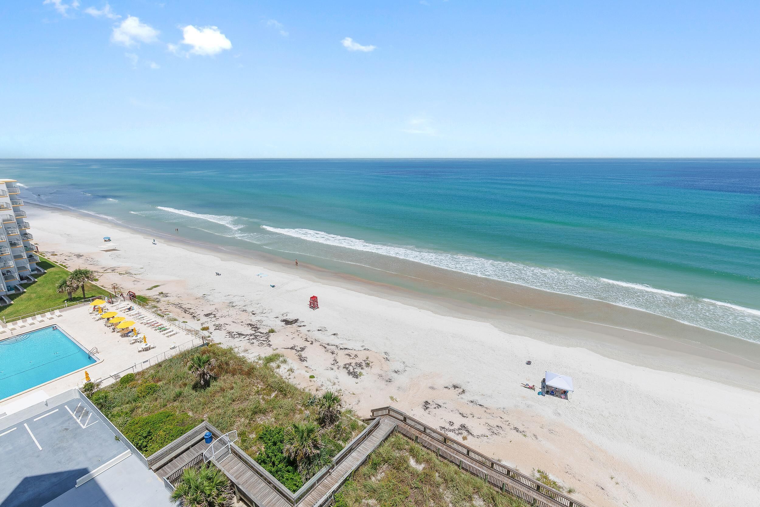 Een strand met een zwembad en een houten looppad.