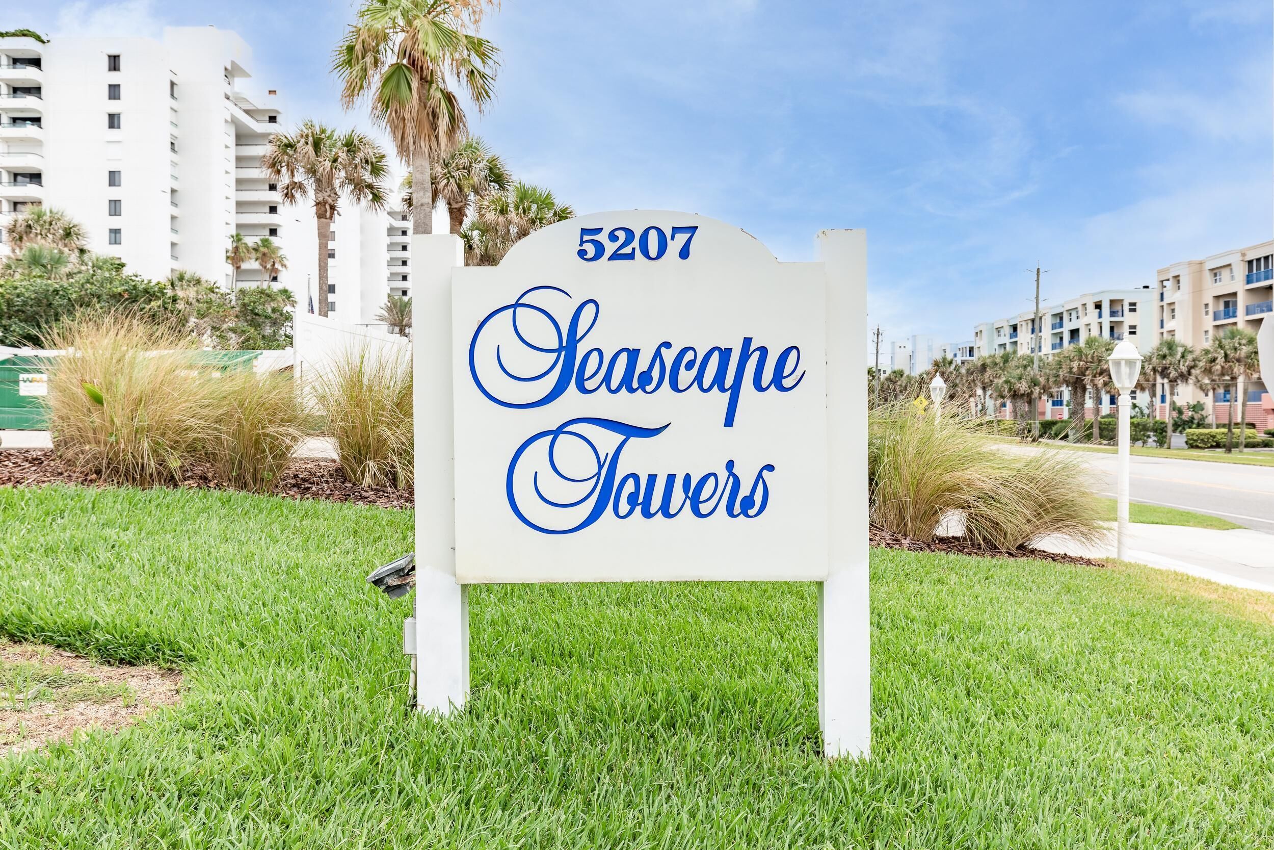 Une enseigne indiquant « Seascape Towers », avec le numéro 5207, entourée d’herbe et de palmiers.