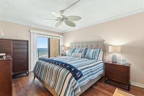 Une chambre à coucher comprenant un lit, une table de chevet, une commode, un ventilateur de plafond et une fenêtre donnant sur un paysage agréable.
