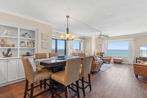 A spacious dining area with a high ceiling, a chandelier, and a view of the ocean through large windows. - Seascape Towers 1025 (New Smyrna Beach)