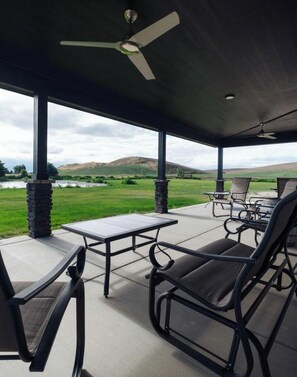 A covered patio with a table and chairs, overlooking a grassy field and hills.